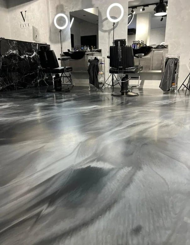 Salon de barbier avec fauteuils noirs sur un sol en résine métallisée grise